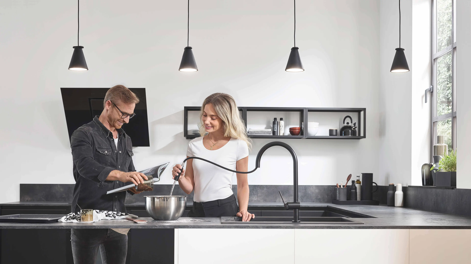 Ein Mann und eine Frau stehen in einer modernen dunklen Küche und befüllen einen Topf